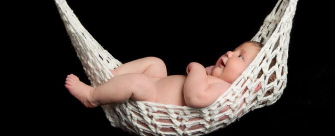 a newborn sleeping in a string hammock against a black background