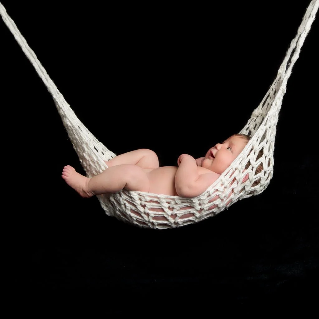 a newborn sleeping in a string hammock against a black background