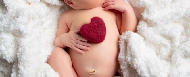 a newborn sleeping on their back on a white blankets holding a felt heart on their chest