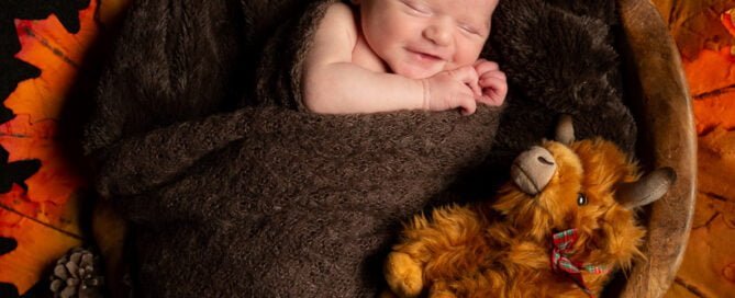 a smiling newborn in my wooden bowl with a stuffed angus cow toy