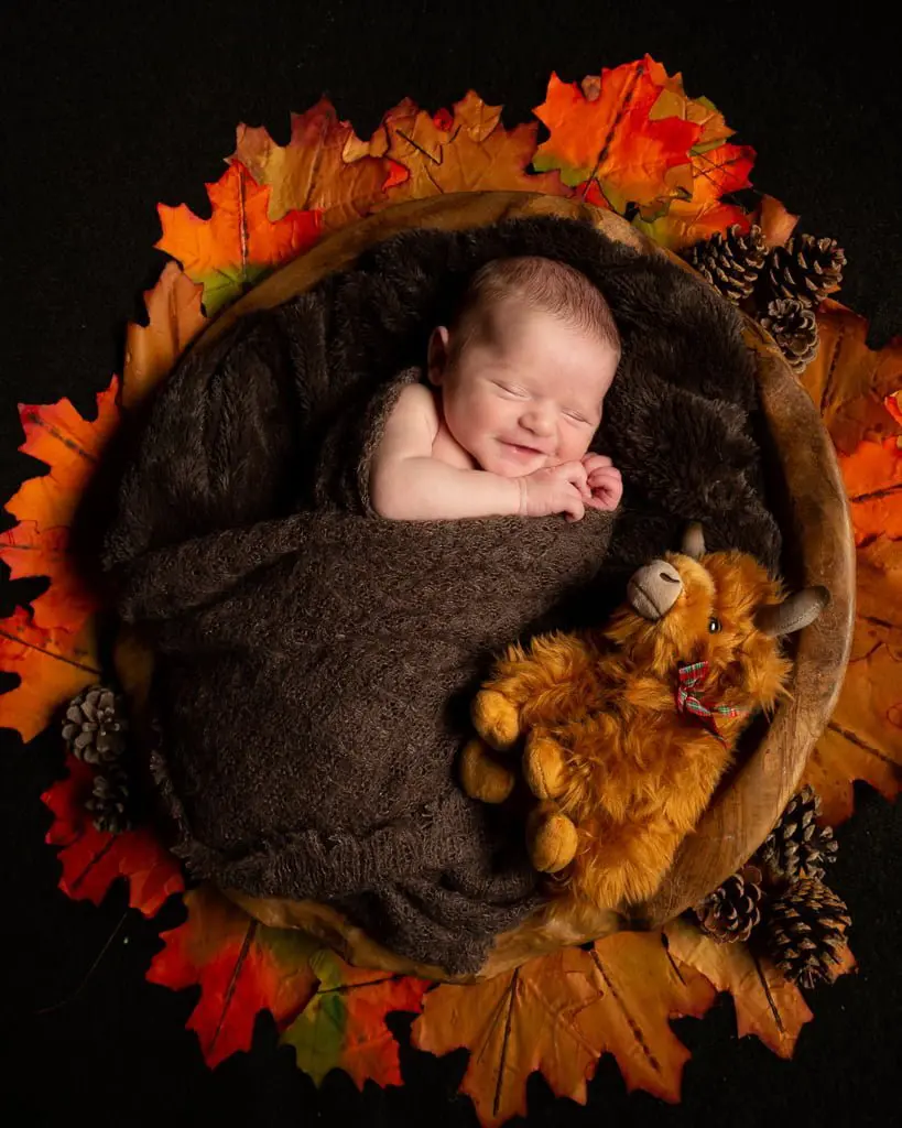a smiling newborn in my wooden bowl with a stuffed angus cow toy