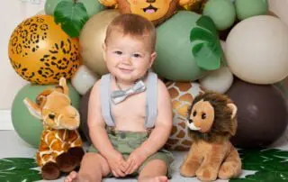a little boy poses in front of jungle themed balloon arrangement