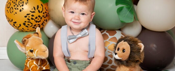 a little boy poses in front of jungle themed balloon arrangement