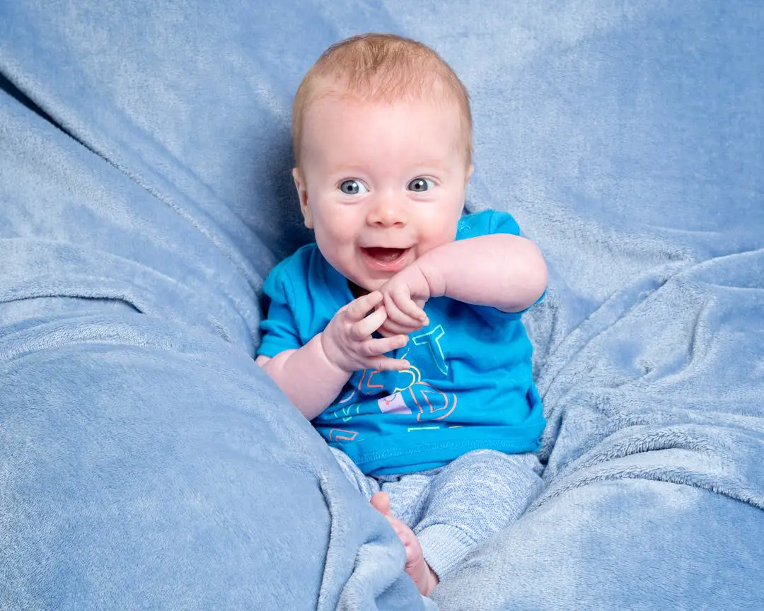 a little boy plays with his hands on a blue blanket