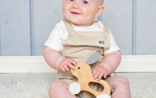 a little boy and a wooden toy against a blue backdrop