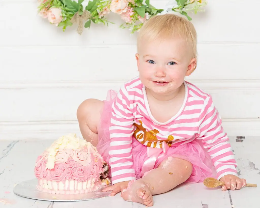  alittle girl dressed in pink stripes sitting beside her cake