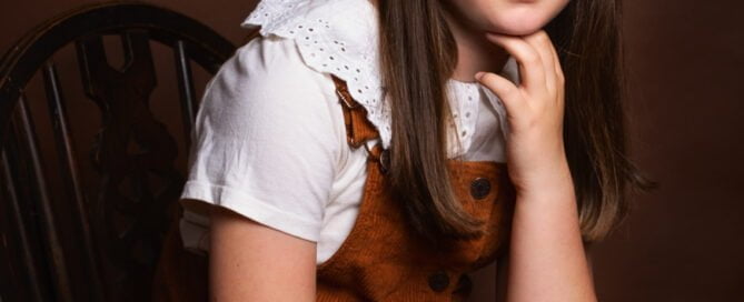 a fine art portrait of a young girl dressed in a brown dress photographed against a brown background