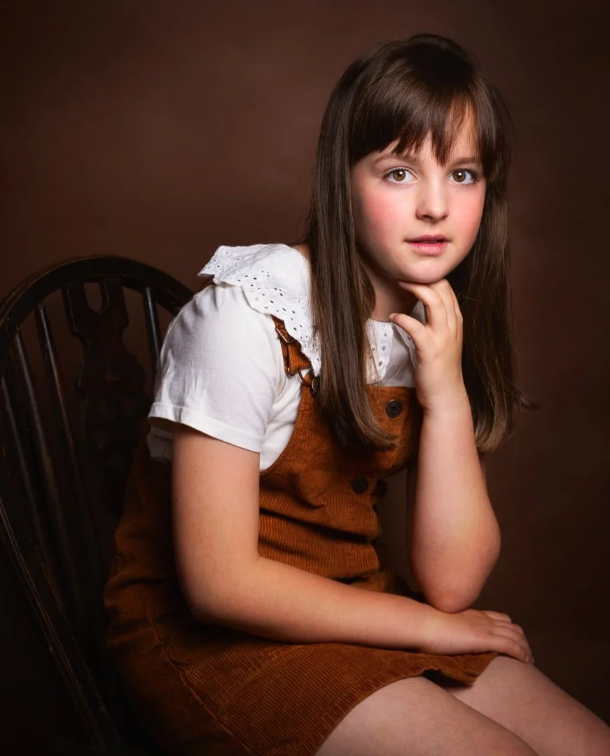 a fine art portrait of a young girl dressed in a brown dress photographed against a brown background