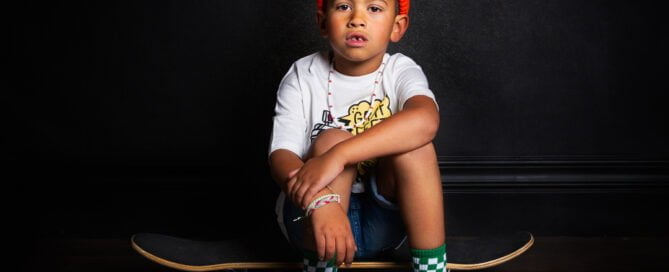 a young boy poses in the studio sitting on a skateboard