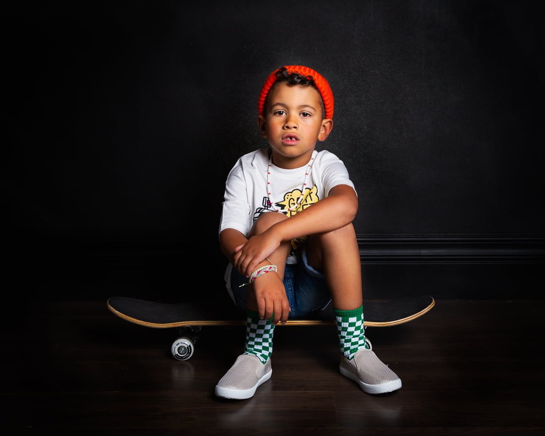 a young boy poses in the studio sitting on a skateboard