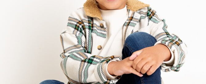 a smiling boy poses for a professional photo in jeans and a jacket