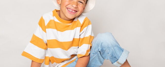 A boy poses smiling in jeans and a stripy tshirt