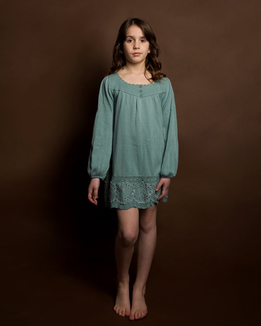 a girl in a green dress poses against a brown background at a fine art photo shoot