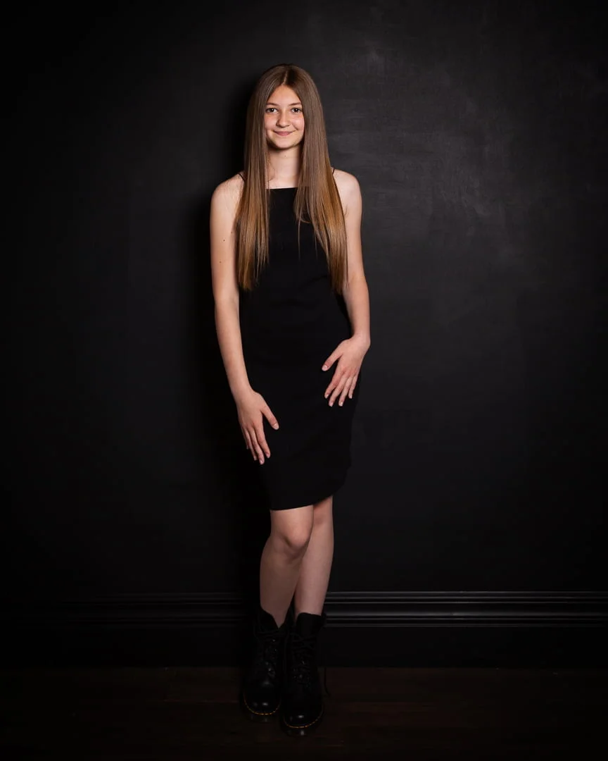 a teen poses for a portrait in a black dress