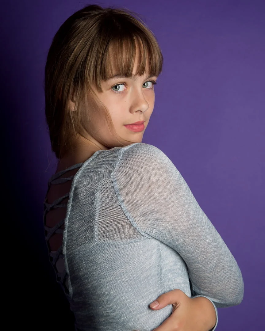 a girl poses in front of a purple background in a fine art portrait