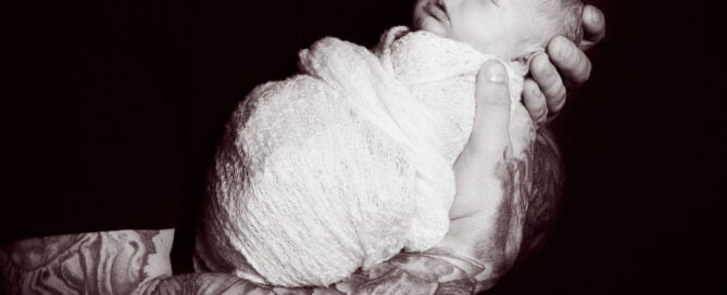 a black and white image of a newborn sleeping in his dads arms