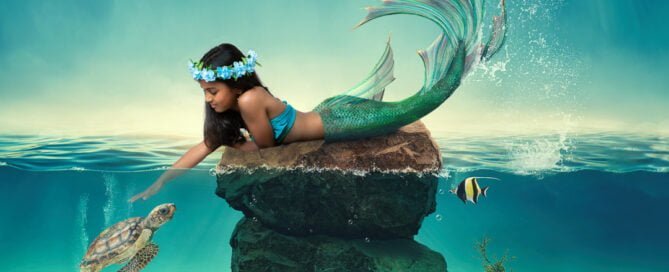 a little girl looks down at a turtle in the ocean at a mermaid photo shoot
