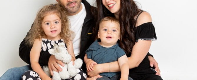 a mum and dad and their two young children sit on the floor and smile for the camera