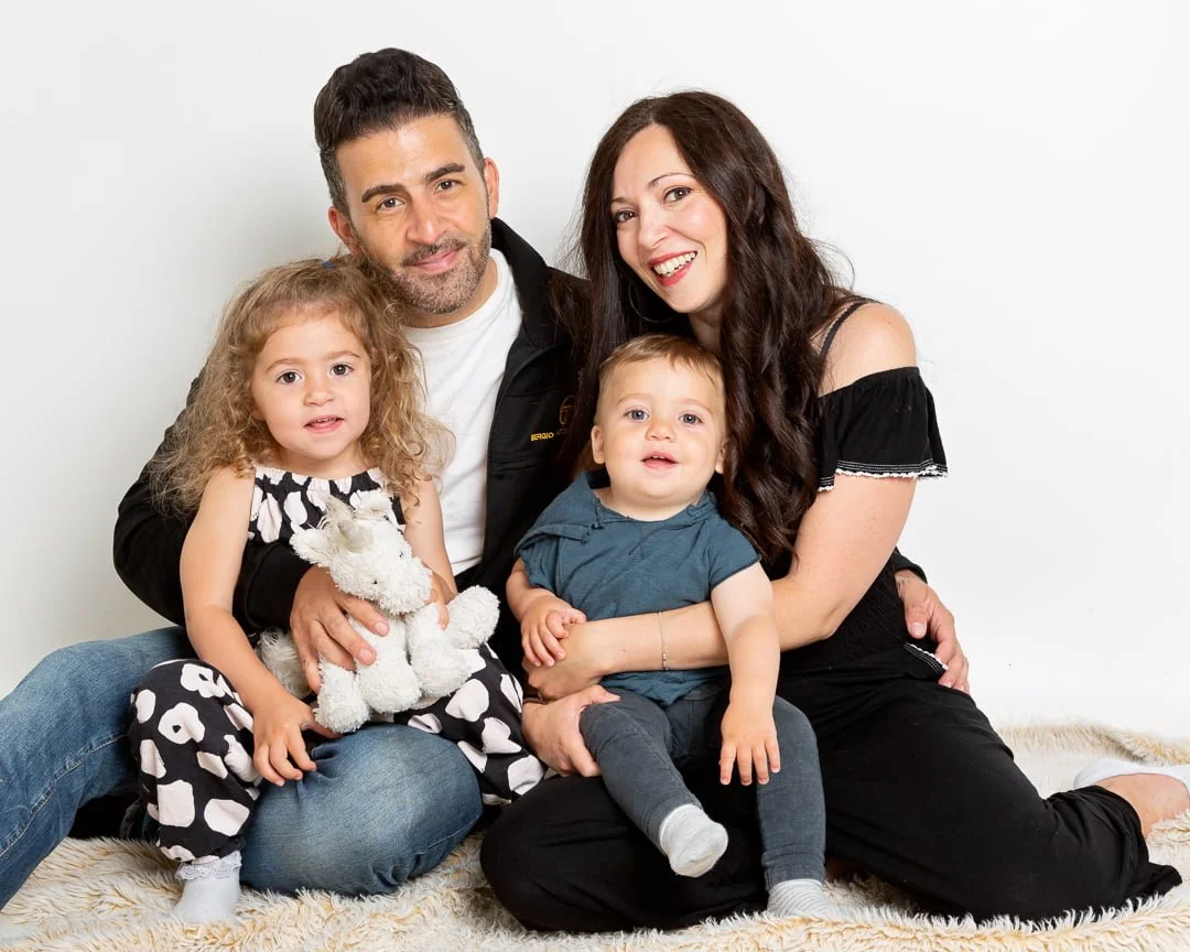 a mum and dad and their two young children sit on the floor and smile for the camera