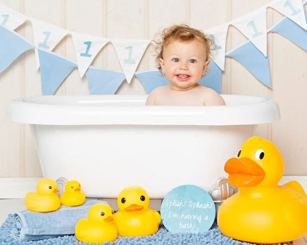a curly haired little boy in a tub surrounded by rubber ducks