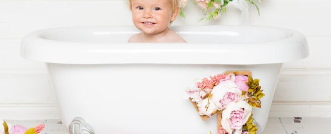 A little girl smiling in a white tub with lots of flowers around her