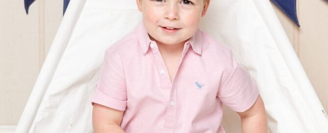a little boy in a pink shirt poses in a miniature teepee