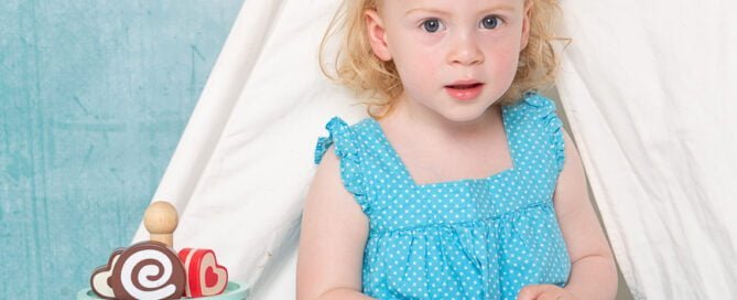 a little girl poses with a teaset and toy cakes