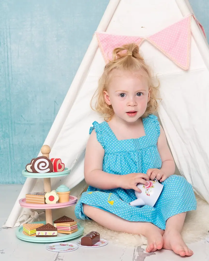 a little girl poses with a teaset and toy cakes
