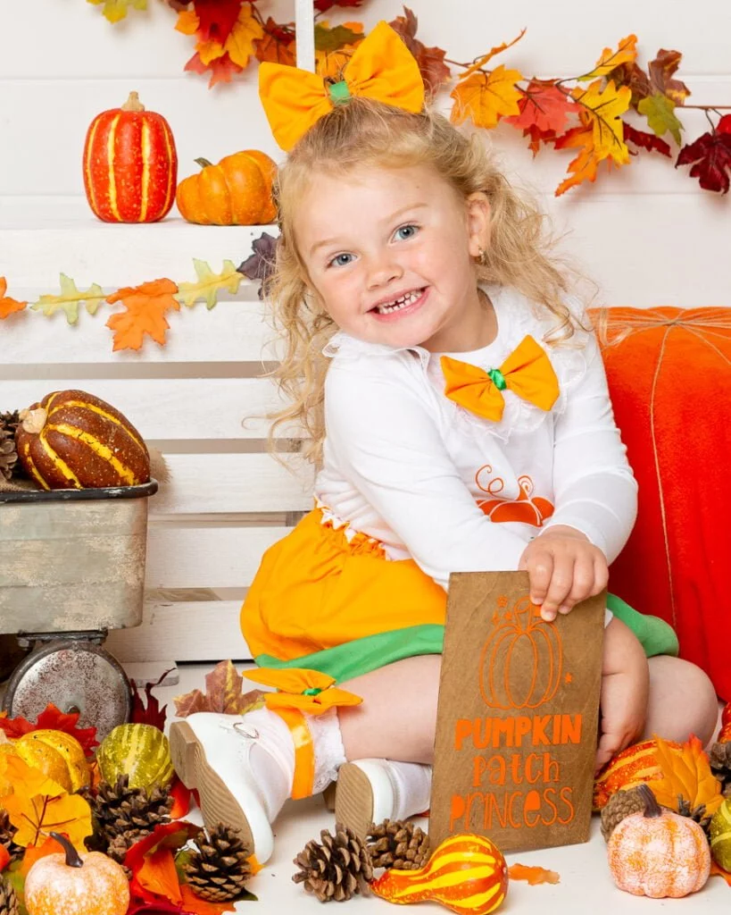 a little girl poses at a pumpkin selling booth at a pumpkin themed photo shoot event