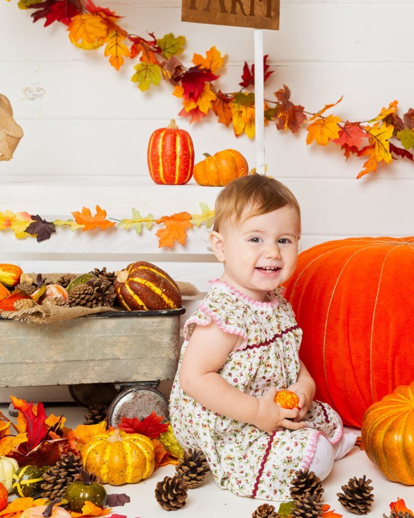 Pumpkin Patch Mini Photo Shoot Event West Sussex a little girl poses with a pumpkin at a pumpkin selling booth at a pumpkin themed photo shoot event