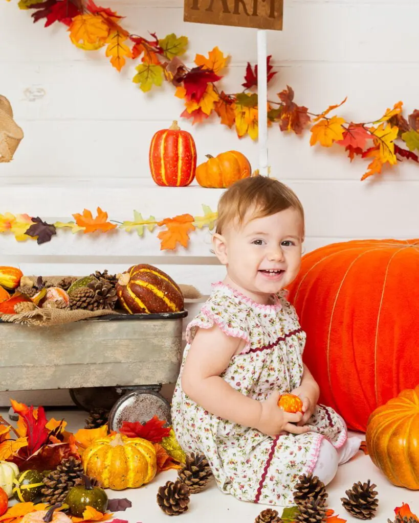 a little girl poses with a pumpkin at a pumpkin selling booth at a pumpkin themed photo shoot event