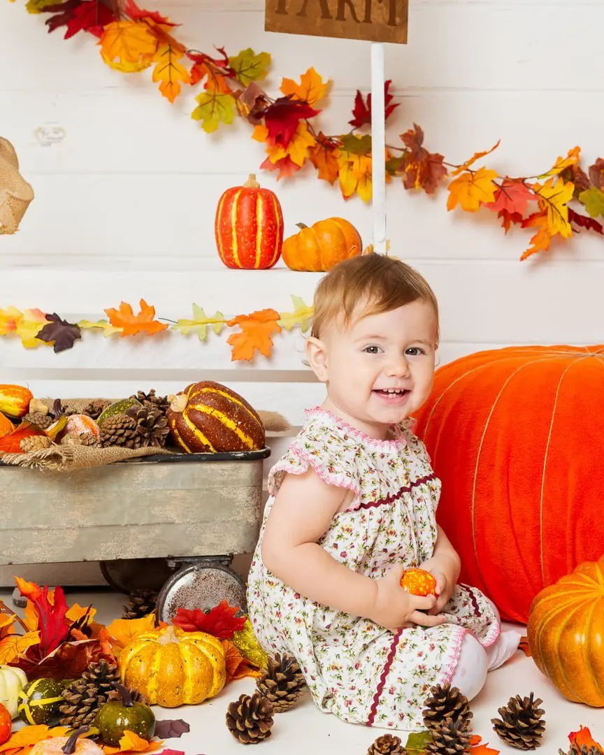 a little girl poses with a pumpkin at a pumpkin selling booth at a pumpkin themed photo shoot event
