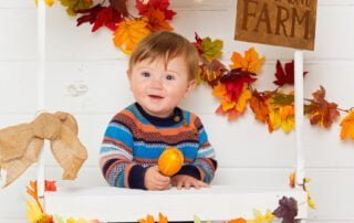 a little boy poses at a pumpkin selling booth at a pumpkin themed photo shoot event