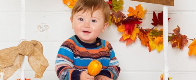 a little boy poses at a pumpkin selling booth at a pumpkin themed photo shoot event