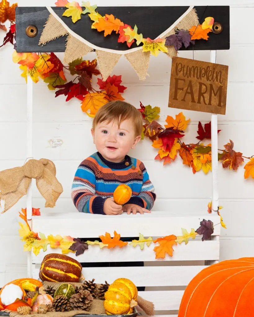 a little boy poses at a pumpkin selling booth at a pumpkin themed photo shoot event