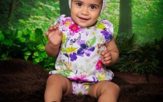 a little girl in a floral outfit poses against a woodland themed background