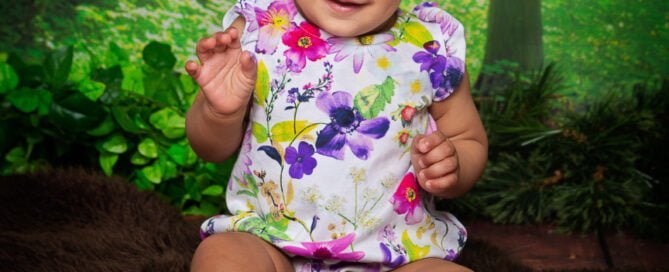 a little girl in a floral outfit poses against a woodland themed background