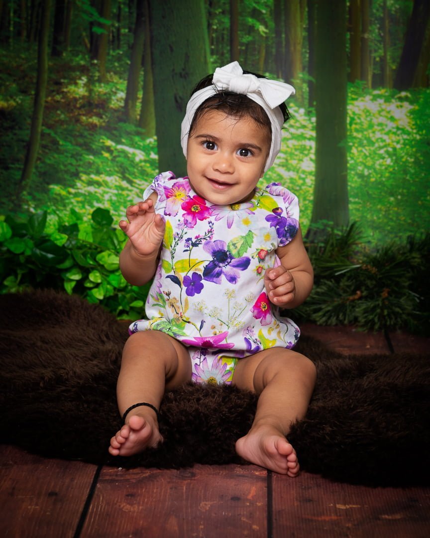 a little girl in a floral outfit poses against a woodland themed background