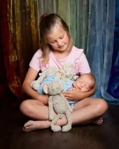 a big sister holds her baby brother against a rainbow curtain