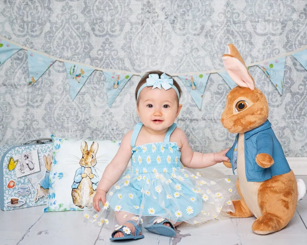 a little girl dressed in blue poses with a large Peter Rabbit toy