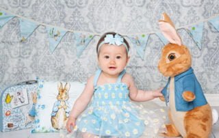 a little girl dressed in blue poses with a large Peter Rabbit toy