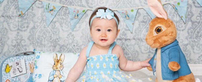 a little girl dressed in blue poses with a large Peter Rabbit toy