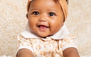 a little girl in a headband poses on a cream fluffy blanket