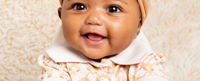 a little girl in a headband poses on a cream fluffy blanket
