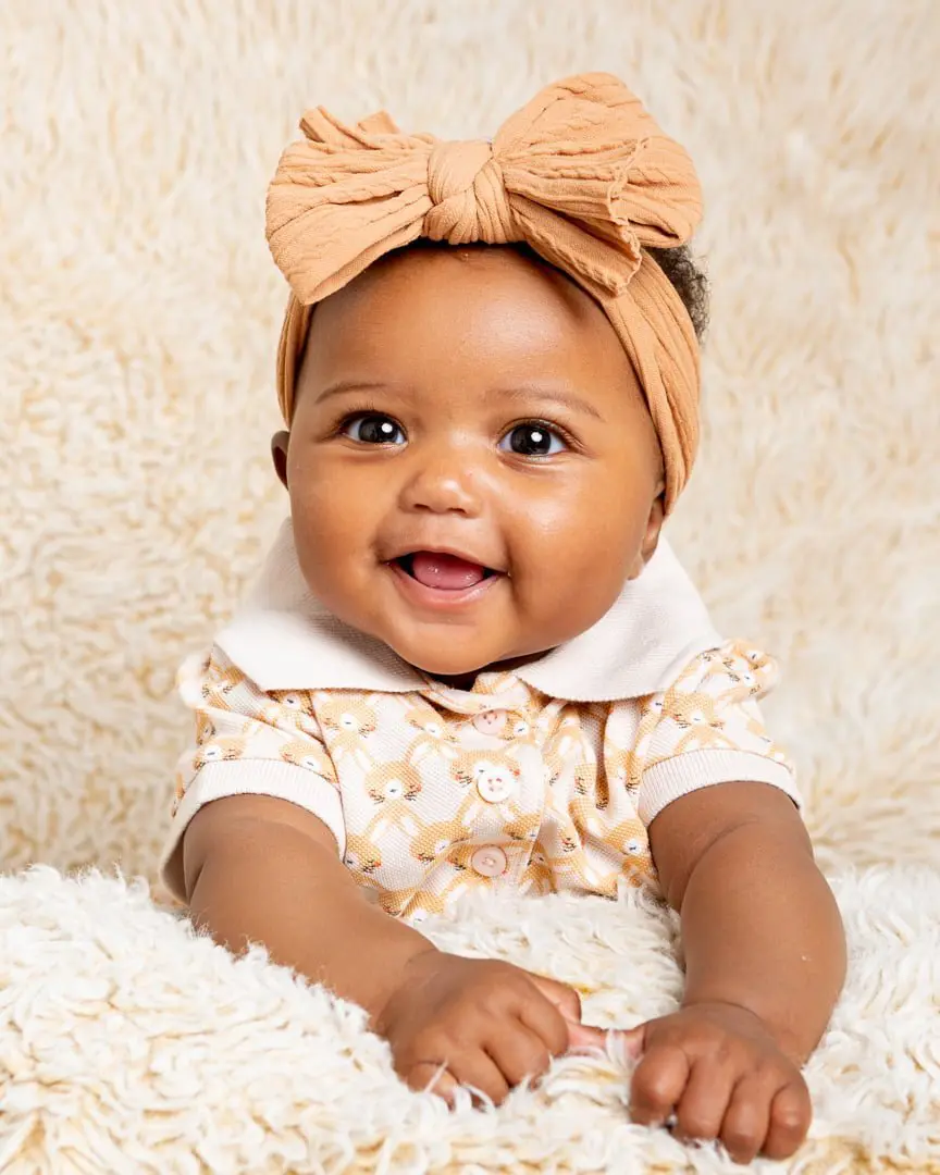 a little girl in a headband poses on a cream fluffy blanket