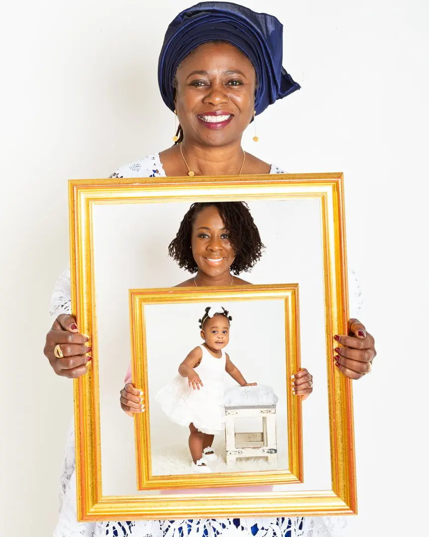 three generations of family pose for a family photo, each holding a frame with a picture of the generation down