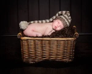 a newborn in a hat sleeping on my prop basket