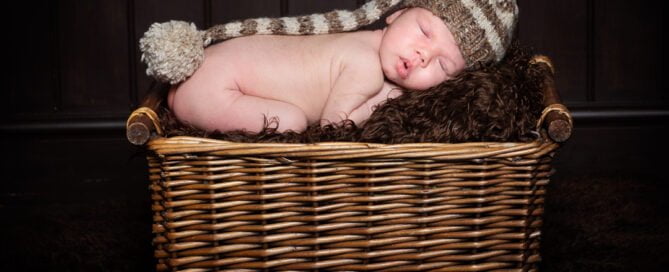 a newborn in a hat sleeping on my prop basket