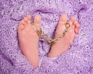 Newborn feet holding a vintage bracelet which was a client's family heirloom