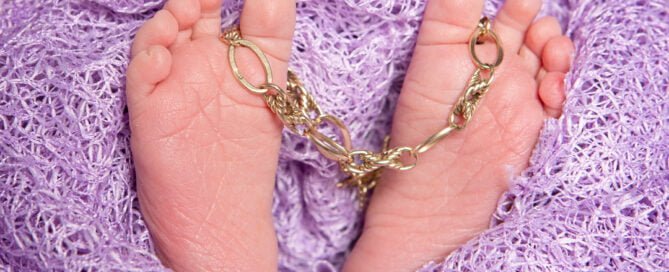 Newborn feet holding a vintage bracelet which was a client's family heirloom